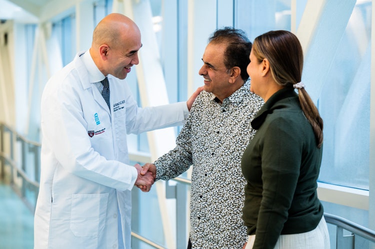 Smiling physician shakes hands with a patient accompanied by a family member in a hospital hallway.
