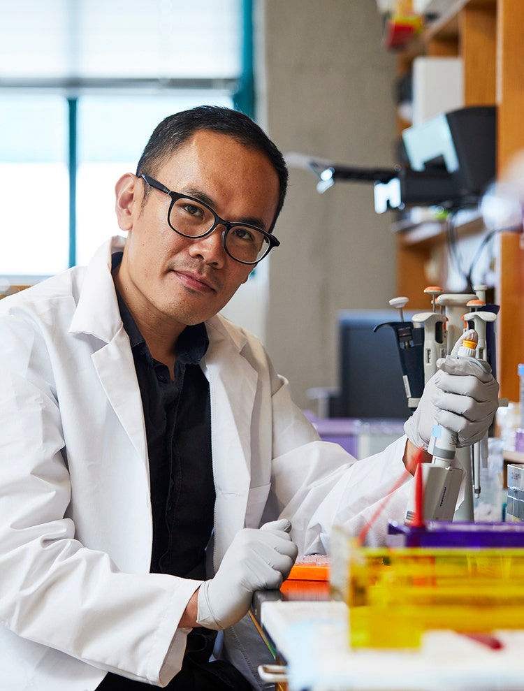 Researcher in a white coat uses a pipette at a laboratory workbench.
