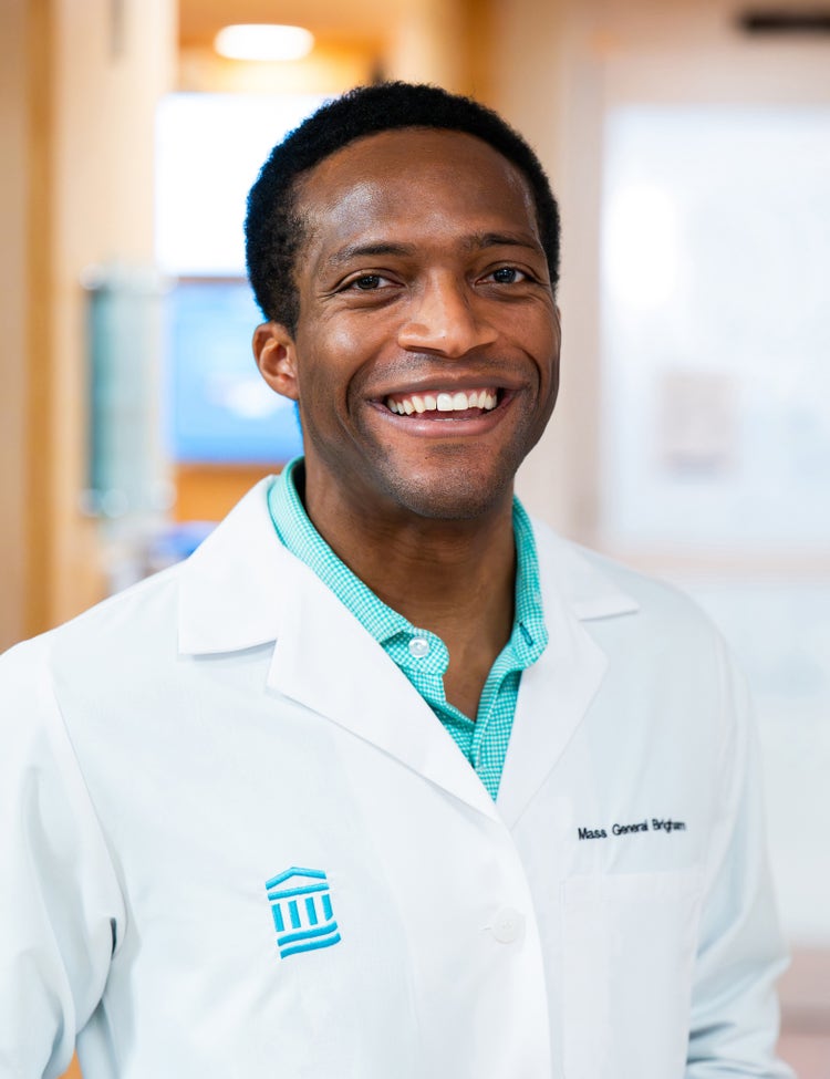 Smiling Mass General Brigham physician wearing a white coat in a hospital hallway.